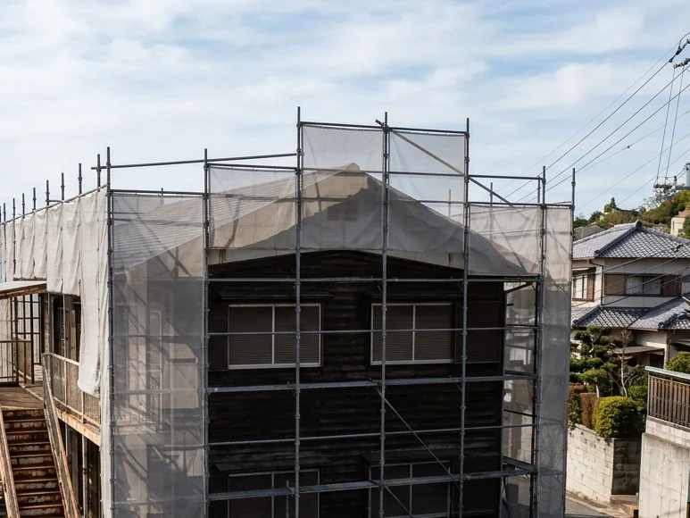 鉄骨の外階段がある2階建ての木造アパートが、足場とメッシュシートで囲まれている様子