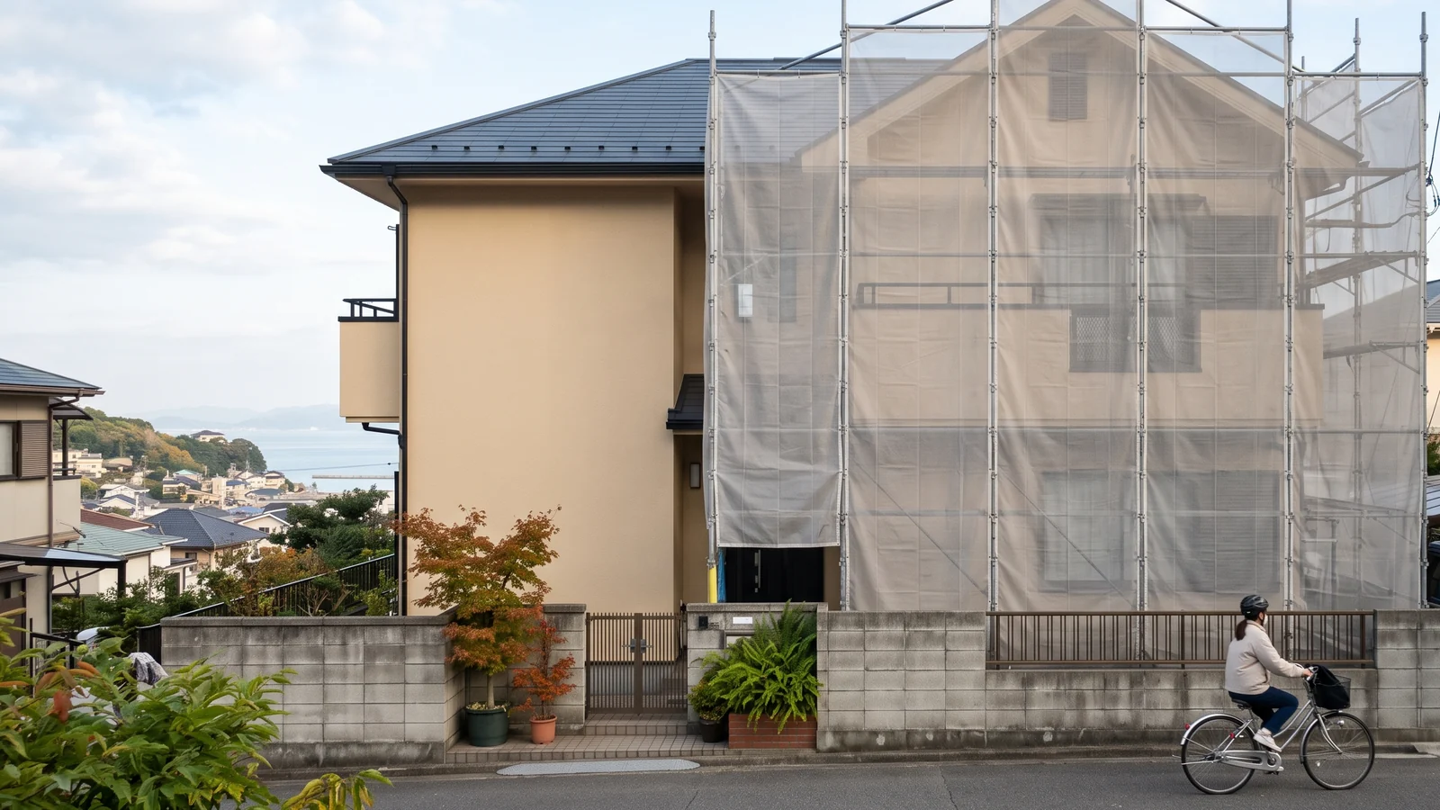 足場と養生ネットに囲まれた戸建て住宅で外壁の塗り替えが進んでいる様子